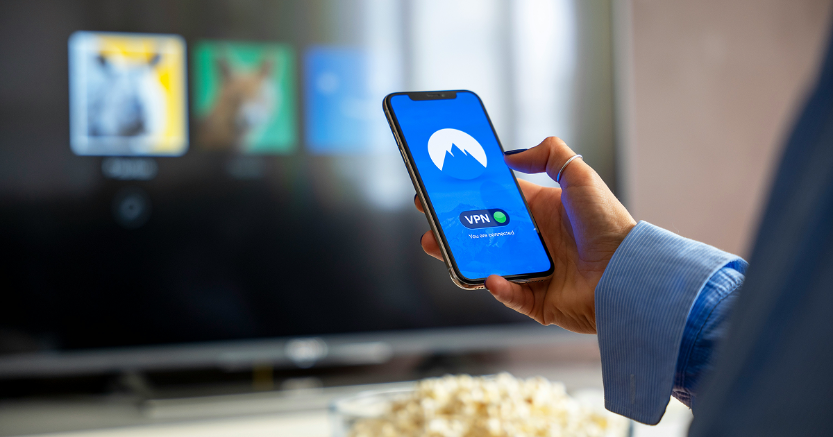テレビ画面の前でVPNアプリを表示したスマートフォンを持つ手元