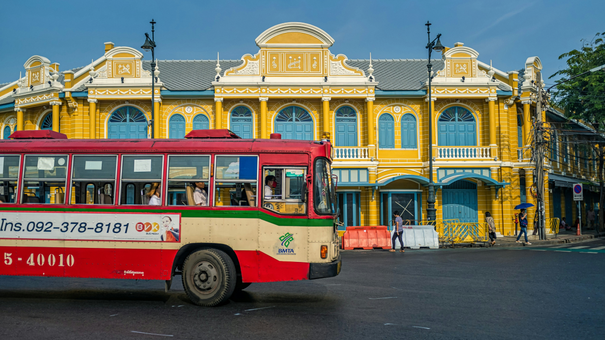 黄色い建物の前を走るバンコクの路線バス