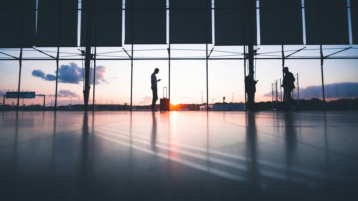空港のガラス張りロビーに立つ旅行客たち