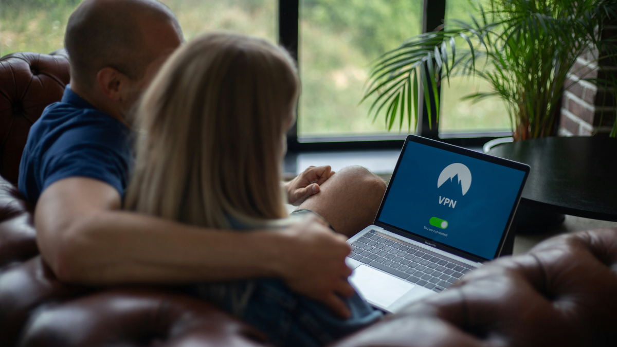 ソファでVPNアプリを表示したノートパソコンを見るカップル